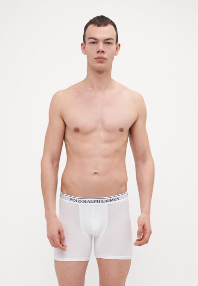 Beli bokserice iz gladkega bombaža, ki imajo elastični pas s ''POLO RALPH LAUREN'' blagovno znamko v mornarsko modri barvi. Prileganje je tesno in krojeno.