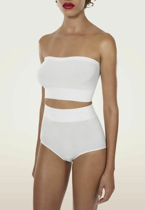 Donna che indossa un top bandeau bianco senza spalline e biancheria intima bianca senza cuciture a vita alta, in piedi davanti a uno sfondo chiaro e semplice.