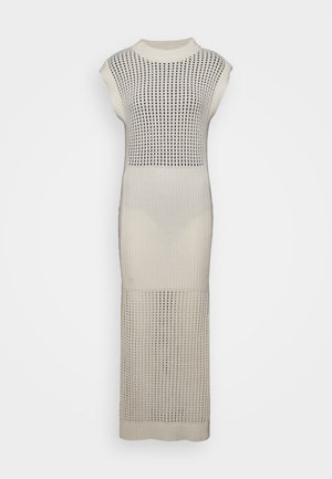 Neulottu valkoinen mekko, jossa on lyhyet hihat ja avoimet neuleosat. Yhdistetty mustiin sandaaleihin ja vihreään, taiteltuun clutch-laukkuun.