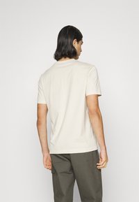 T-shirt beige à manches courtes en coton doux avec un col rond. Il présente une texture lisse et un design simple. Vue de dos montrée.