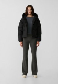 Doudoune noire avec capuche, fermeture éclair à l'avant et rembourrage ; haut gris à manches longues ; pantalon gris évasé ; baskets crème.