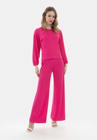 Completo fucsia a due pezzi composto da una maglietta a maniche lunghe con scollatura a girocollo e pantaloni a gamba larga coordinati. Tessuto morbido con vestibilità rilassata.