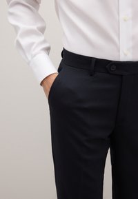 Wit shirt met lange mouwen gecombineerd met donkerblauwe, gestructureerde broek met zakken en knoopsluiting, voor een formele uitstraling.