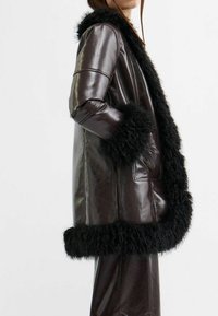 Bruine faux leren jas met zwarte bontafwerking, met een ontspannen pasvorm, lange mouwen, twee voorzakken en een gladde, glanzende textuur.