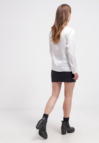 Vit satin långärmad topp i kombination med en svart minikjol, bärs med svarta ankelstövlar. Slät textur och åtsittande design.