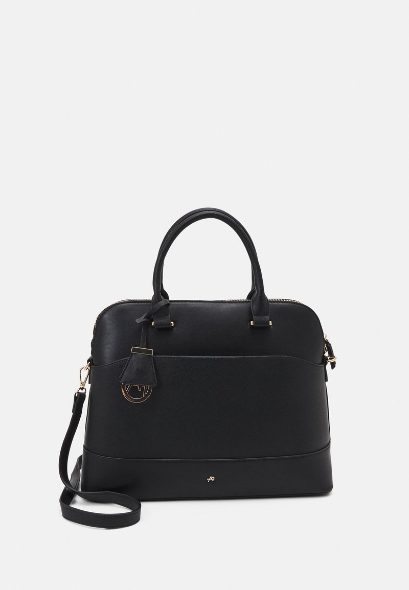 Sac à main en cuir noir avec doubles anses, poche avant, bandoulière amovible et ferrures dorées sur un fond clair uni.