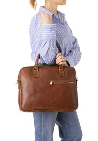 Sac à ordinateur en cuir marron avec deux poignées courtes, doté d'une poche zippée à l'avant et d'accents carrés. Le sac a une texture lisse et une forme structurée.