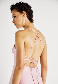 Ροζ σατέν φόρεμα με λεπτές διασταυρούμενες τιράντες και κορδόνι στο πίσω μέρος. Η λεία υφή και το εφαρμοστό σχέδιο αναδεικνύουν τη σιλουέτα.