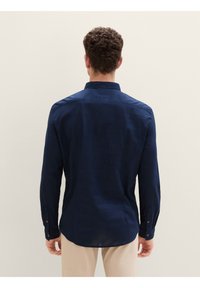Camisa de manga larga azul marino con cuello abotonado, tela texturizada y puños abotonados. La camisa tiene un dobladillo curvado y un yugo trasero.