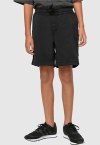 Shorts de sport noirs avec une taille élastique et un cordon de serrage ajustable. Comprend des poches latérales et une coupe détendue. Portés avec des chaussures de course noires.