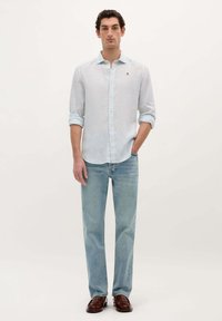 Cămașă button-up cu dungi bleu deschis, cu mâneci lungi, asortată cu blugi bleu deschis și pantofi din piele maro. Design simplu și curat.