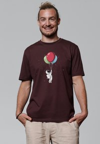 Bordeauxrood T-shirt met een afbeelding van een astronaut die kleurrijke ballonnetjes vasthoudt. Gemaakt van katoen, met een ontspannen pasvorm en korte mouwen.