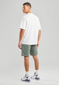 White cotton t-shirt paired with olive green shorts. Textured fabric, short sleeves, crew neckline, worn with white and blue sneakers.