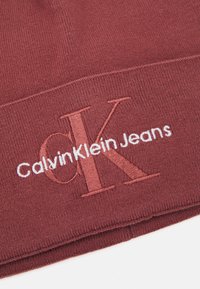Burgundi kötött sapka hajtott mandzsettával, fehér hímzett 'CalvinKlein Jeans' logóval. Puha tapintás és kényelmes illeszkedés.