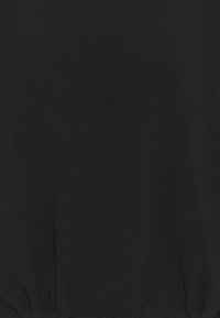 Nahaufnahme von schwarzem Stoff mit gerafftem Elastikdetail am unteren Rand, das Textur und Nähte zeigt.