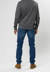 Sudadera gris de mangas largas y cuello redondo, combinada con jeans azul de lavado medio y botas marrones hasta el tobillo, vista desde la parte de atrás.