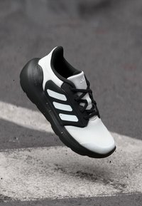 Sneaker bianco e nero con tomaia in mesh traspirante, suola nera spessa, tre strisce bianche e lacci neri. La suola intermedia presenta una finitura testurizzata.