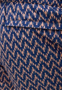 Tkanina w wzór homara, z ciemnoniebieskim tłem i różowymi homarami. Gładka tekstura, elastyczny pasek w talii oraz detal w postaci kieszeni z tyłu.