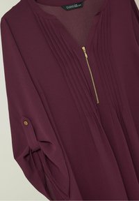 Blouse à manches longues prune avec plis sur le devant, fermeture éclair dorée et détail de manche à bouton de la marque Evans en taille UK 18/EUR 46/US 14.