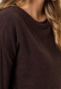 Pull en tricot marron avec un col rond, une texture douce et un léger tombé aux épaules, sans motifs ni détails métalliques visibles.