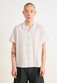 Chemise à manches courtes rayée en beige clair et blanc, dotée d'un col, de six boutons et d'une poche poitrine ; tissu en coton avec une texture douce.