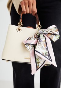 Borsa a mano di tessuto crema con manici in pelle marrone, dotata di una sciarpa in seta decorativa in colori pastello e accenti in stampa animale. Logo visibile.