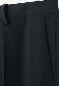 Część czarnych, dopasowanych spodni pokazująca pas, szlufkę na pasek, kieszeń w szwie bocznym oraz gładką fakturę tkaniny.