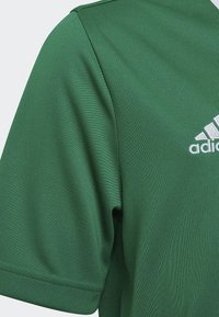Camiseta deportiva verde hecha de tejido texturizado, con cuello redondo, mangas cortas y un logo bordado en blanco en el pecho.