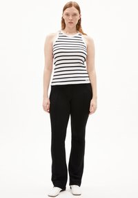 Top senza maniche a righe bianco e nero, abbinato a pantaloni neri attillati e scarpe bianche; texture liscia, stile casual.