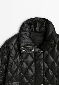 Czarna pikowana kurtka z wysokim, wyściełanym kołnierzem, zatrzaskami, suwakiem i kieszenią na jednolitym białym tle.