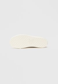 Sole of a shoe, textured with small pyramidal patterns, predominantly white with a subtle embossed logo, curved design.