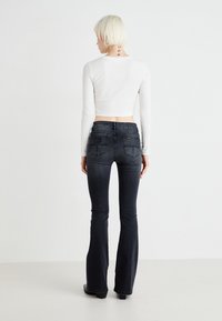 Dark denim flared jeans with a mid-rise waist and rear pockets. Paired with a fitted white long-sleeve crop top, showcasing a smooth texture.