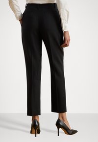 Fekete, egyenes szabású nadrág hátsó zsebekkel, fekete magassarkú cipővel, amelyeken diszkrét részletek találhatók.