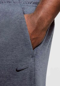 Pantalones deportivos grises hechos de tela texturizada, con un bolsillo lateral y un pequeño logo negro de Nike en la parte delantera.