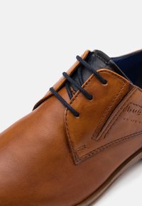 Chaussure en cuir brun avec des accents noirs, dotée de lacets ronds, d'une texture lisse et de coutures sur les côtés pour une touche de design supplémentaire.