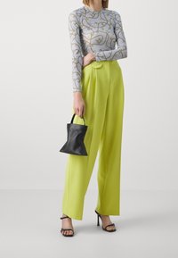 Vaaleanharmaa pitkähihaisuus, jossa on kultaketjumainen kuvio, yhdistettynä korkeavyötäröisiin kirkkaankeltaisiin housuihin, ja hän pitää pientä mustaa laukku.