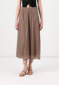 Jupe midi marron avec un motif texturé de losanges en relief. Taille élastique, tissu léger et silhouette fluide. Accompagnée de talons à lanières.