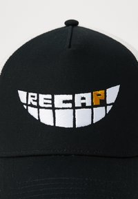 Black baseball cap with a structured crown features white and gold embroidery. The design includes a smile-like motif with the text "RECAP."