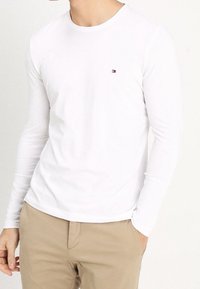 Bílý dlouhý rukáv tričko vyrobené z bavlny, s kulatým výstřihem a malým, barevným logem na levé hrudi.