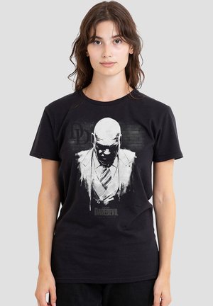 Young woman wearing black T-shirt with monochrome graphic of bald man in suit and tie with "Daredevil" text below.