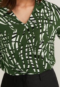 Blusa verde a fantasia con scollo a V, caratterizzata da design astratti ondulati in verde, bianco e nero. Tessuto liscio con vestibilità ampia.