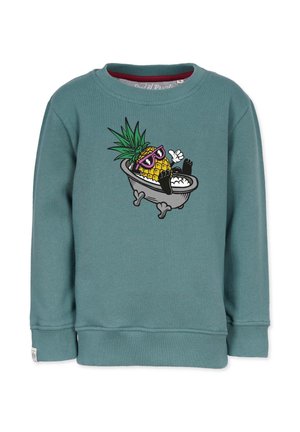 Turkis sweater med grafik af en ananas med solbriller, der slapper af i et fritstående badekar fyldt med bobler.