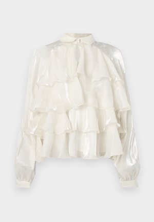 Blouse blanche transparente avec volants superposés, manches longues bouffantes avec poignets, et petit col avec fermeture à bouton au niveau du cou.