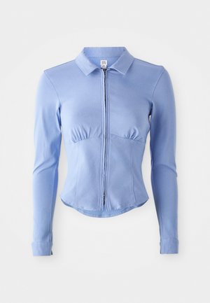 Light blue long-sleeve zip-up shirt with a collared neck, fitted design, and gathered detailing at the bust, made from a stretchy fabric.