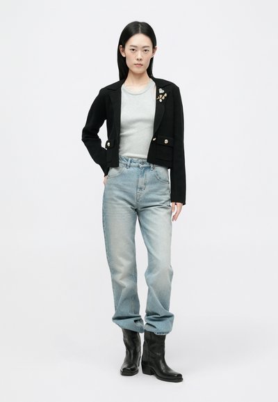 Μαύρο κομμένο σακάκι με χρυσά κουμπιά, γκρι μπλούζα, ανοιχτό μπλε φαρδιά τζιν και μαύρες ankle μπότες. Περιλαμβάνει διακοσμητικό μπροστά στον σακάκι.