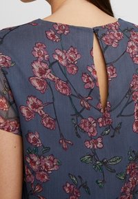 Blue floral-patterned dress with sheer sleeves, featuring pink blossoms and green leaves. Keyhole detail at the back for added design interest.
