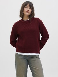 Sweater de malha bordeaux com decote redondo, com um padrão texturizado em nervuras, e mangas longas, sobre uma camisa branca, combinado com calças de ganga claras.
