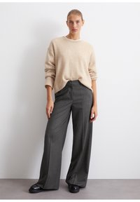 Beige strikkegenser med en løs passform og ribbede mansjetter, kombinert med mørkegrå bukser med pinstriper og svarte sko.