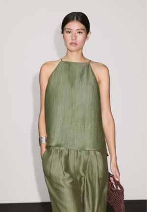 Green linen halter top with a relaxed fit, featuring textured fabric and a slightly curved hem, paired with matching pants and a burgundy bag.