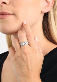 Anello in argento con un motivo a zigzag testurizzato. Finitura liscia, fascia ampia, indossato sull'indice, mette in risalto il design intricato.
